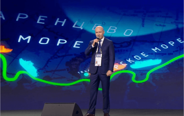 Мужчина в костюме делает доклад на сцене с микрофоном